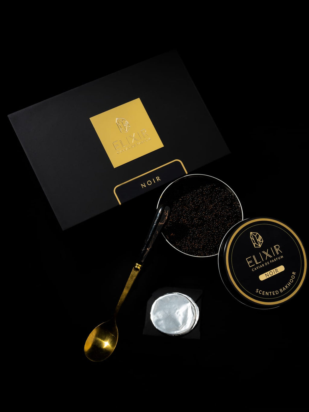 The Noir box open on black, the tin of pearls beside it and a gold spoon lifting a measure