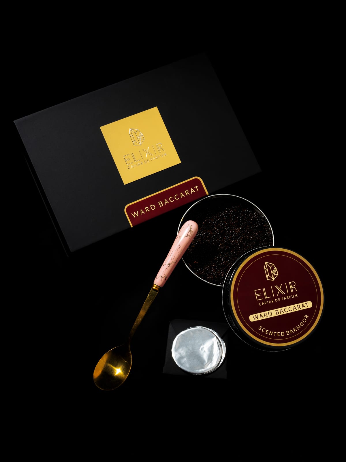 The Ward Baccarat box open on black, its burgundy-lidded tin and a spoon of pearls